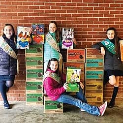 4 girls in front of boxes full of Girl Scout Cookies