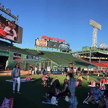 Image of the baseball outfield at Fenway Park with large group of people picnicking in the grass.