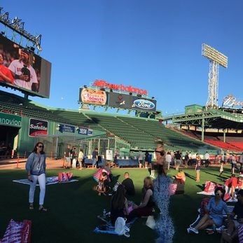 Image of the baseball outfield at Fenway Park with large group of people picnicking in the grass.