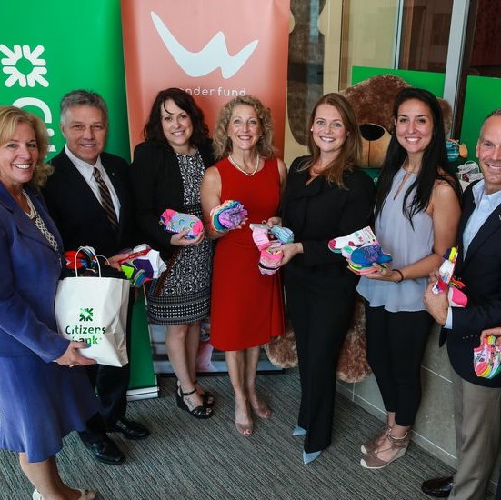 Group of people including First Lady Lauren Baker standing in front of Citizens Bank and Wonderfund sign, holding socks.