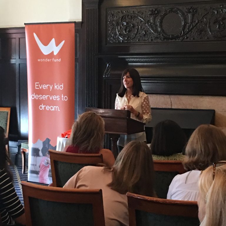 Photo of woman speaking from podium in front of Wonderfund sign.